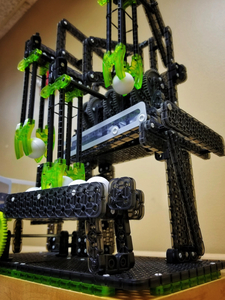 An image shows ball contraption made with a VEX, a robotics building tool. The contraption has several clawed arms that drop down to pick up small white balls.