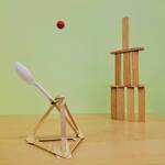 A catapult made of popsicle sticks and a spoon launches a ball at a wooden block tower.