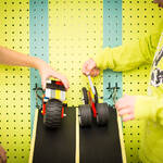 Two children are holding LEGO cars at the top of a ramp, about to release them.