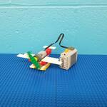 A lego WeDo Plane on a blue background. The green plane propeller is blurred in motion.